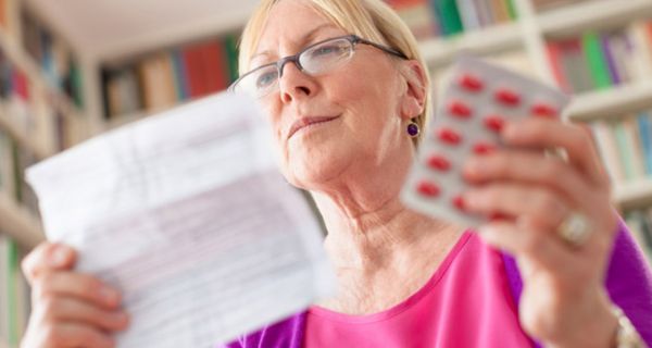 Ältere Frau hat einen Blister mit Kapseln in der Hand und liest einen Beipackzettel