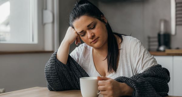 Frau, sitzt müde mit einer Tasse Kaffee am Tisch.