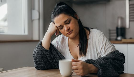 Frau, sitzt müde mit einer Tasse Kaffee am Tisch.