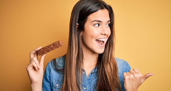 Eine Frau hat einen Proteinriegel in der Hand und freut sich.