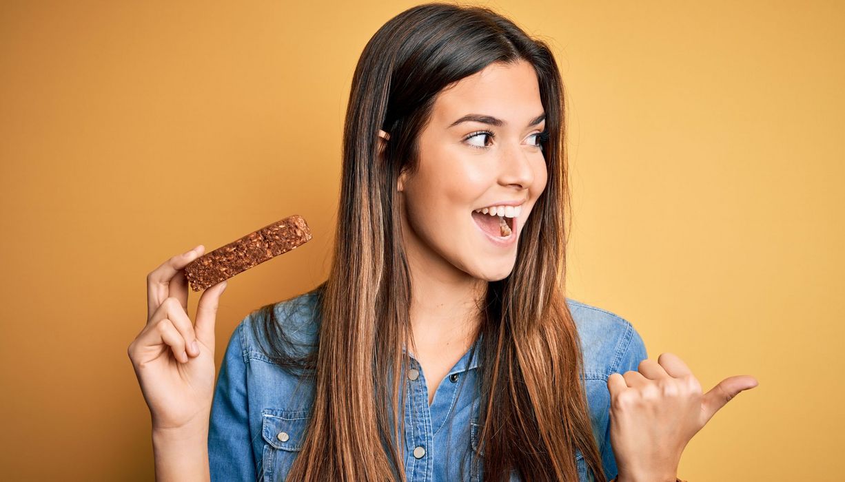 Eine Frau hat einen Proteinriegel in der Hand und freut sich.