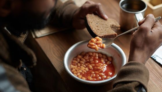 Mann isst gebackene Bohnen mit einem Kanten Brot.
