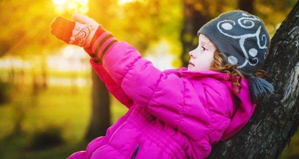 Mädchen, ca. 7 Jahre, zyklamfarbener Anorak, blauweiße Mütze, im Herbstabendlicht an einen Baum gelehnt