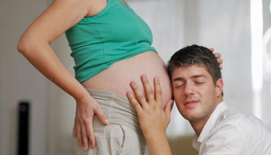 Werdender Vater horcht am kugelrunden Bauch seiner schwangeren Frau