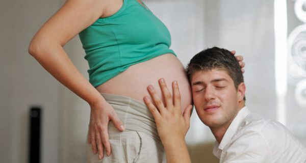 Werdender Vater horcht am kugelrunden Bauch seiner schwangeren Frau