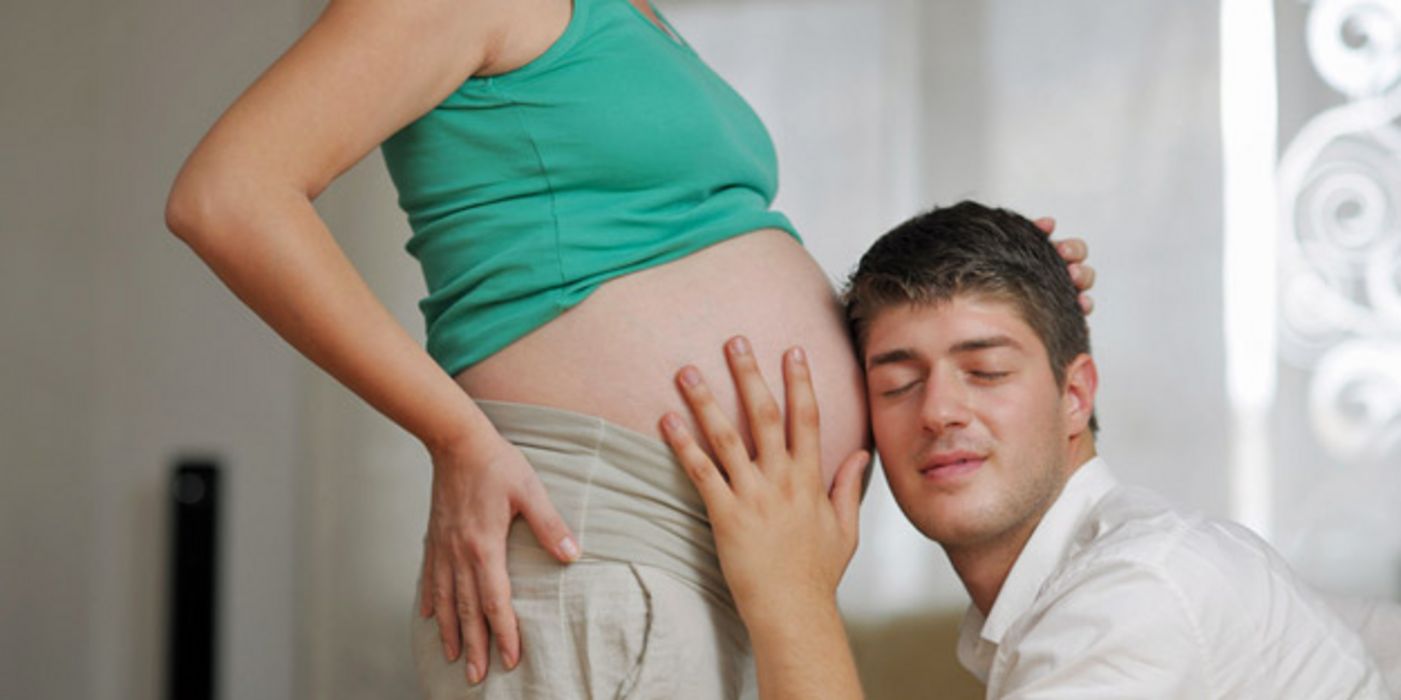Werdender Vater horcht am kugelrunden Bauch seiner schwangeren Frau