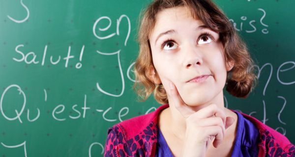 Frontalfoto Schülerin, ca. 11 Jahre, vor Tafel mit französischen Vokabeln, ein Finger im Gesicht, denkt nach, Augen nach oben gerichtet