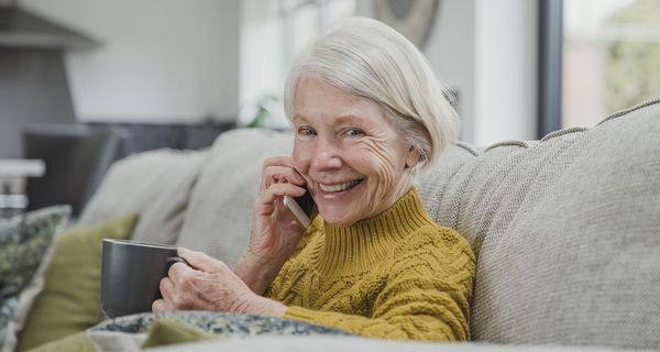 Seniorin mit Kaffee telefoniert auf dem Sofa.