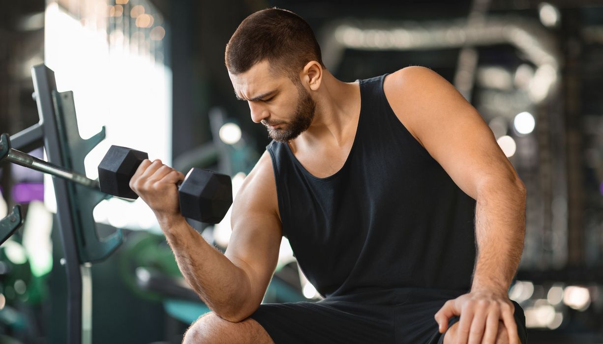 Ein Mann sitzt in einem Fitnessstudio und trainiert seinen Arm.