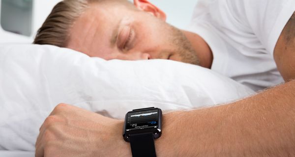 Ein Mann schläaft mit einer Smartwatch am Handgelenk.