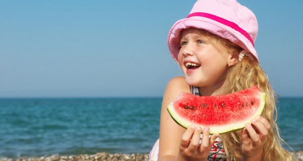 Mädchen liegt am Strand und isst ein Stück Wassermelone