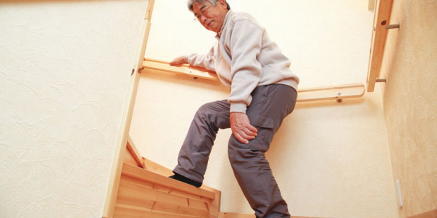 Asiatischer Senior steigt eine Treppe hinauf und hält sich die Hand ans schmerzende Knie