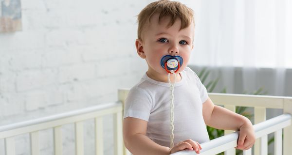 Kleinkind mit Schnuller im Mund im Bett.