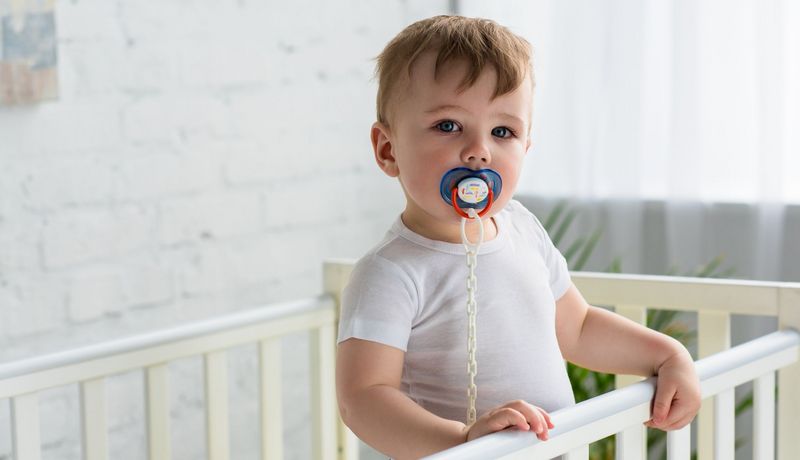 Kleinkind mit Schnuller im Mund im Bett.