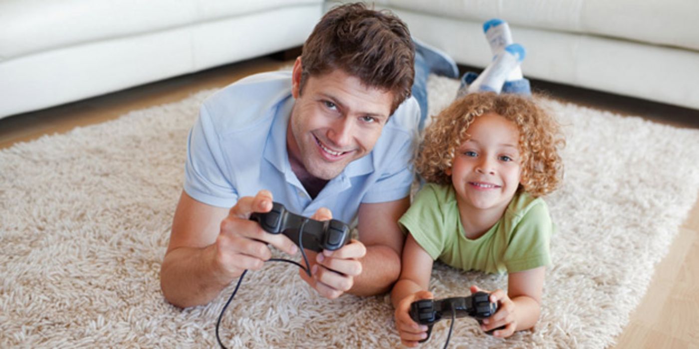 Junger Vater und kleiner Sohn liegen bäuchlings auf dem Teppich und spielen ein Videospiel