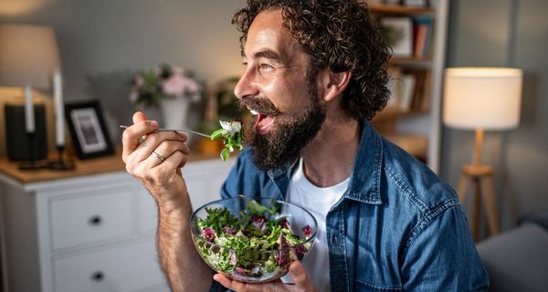 Mann isst aus einer Glasschüssel Salat.