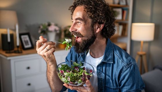 Mann isst aus einer Glasschüssel Salat.