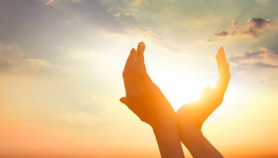 Zwei Hände formen einen Kreis um die Sonne am Himmel.