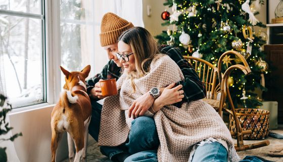 Ein Pärchen sitzt neben einem Hund vor einem Weihnachtsbaum.