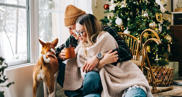 Ein Pärchen sitzt neben einem Hund vor einem Weihnachtsbaum.