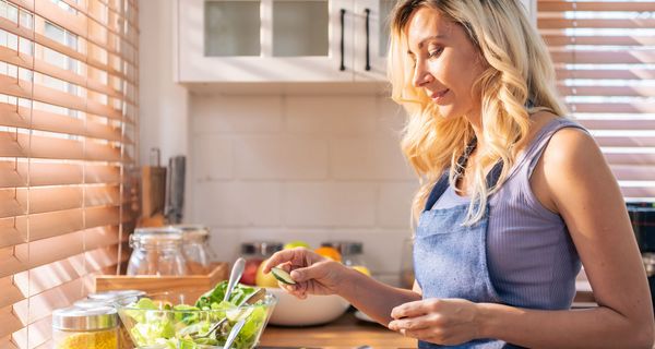 Junge Frau bereitet mäßig begeistert einen Salat zu.