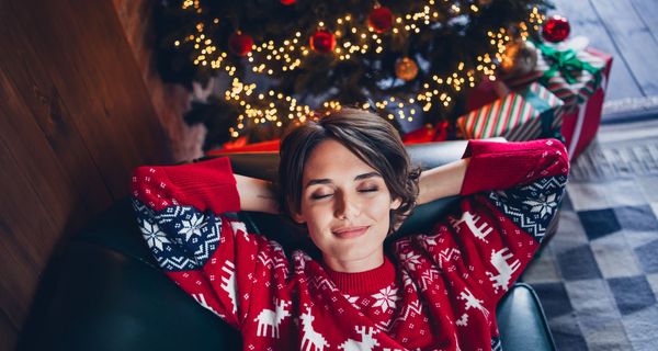 Frau auf dem Sofa vor einem Weihnachtsbaum.
