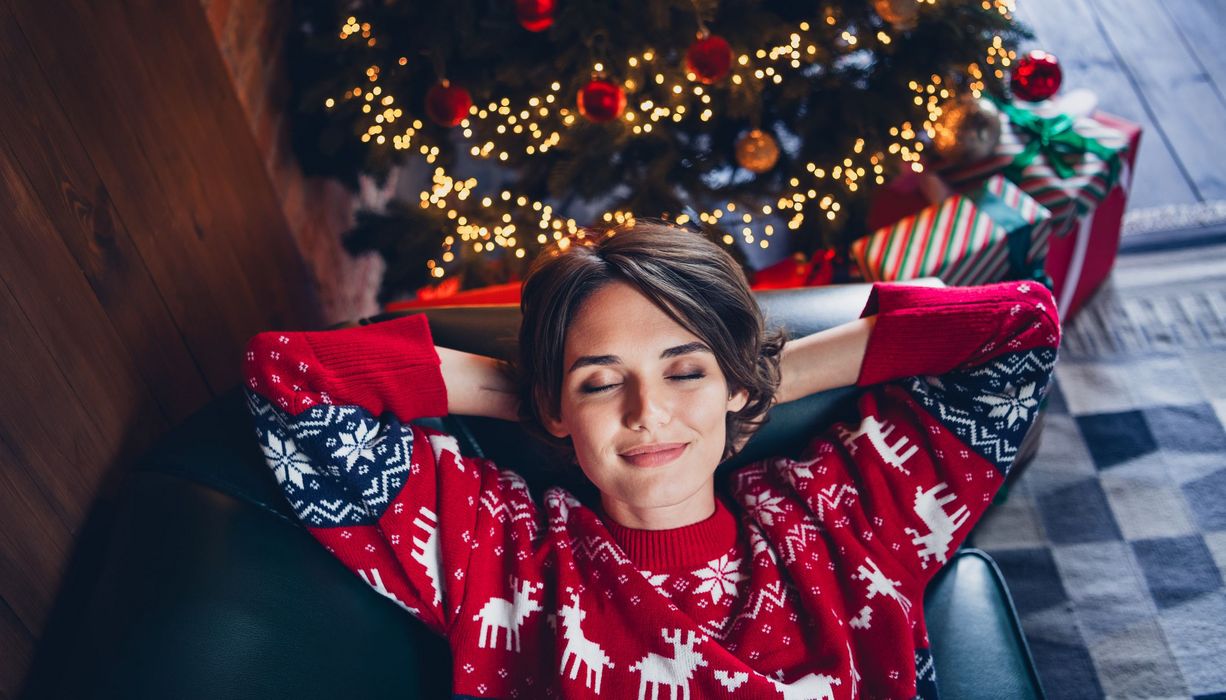 Frau auf dem Sofa vor einem Weihnachtsbaum.