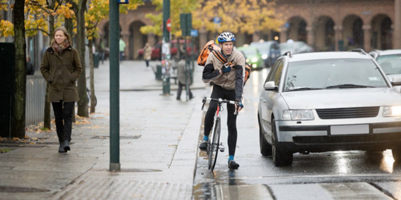 Fahrradfahrer und Autofahrer stehen an einer roten Ampel