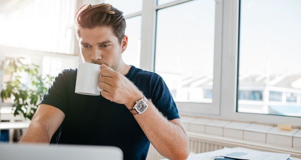 Junger Mann im Büro trinkt eine Tasse Kaffee.