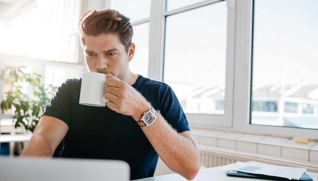 Junger Mann im Büro trinkt eine Tasse Kaffee.