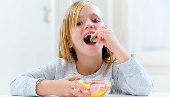 Ein Kind isst ein grünes Fruchtgummi aus einer Schale. 