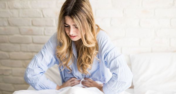 Junge Frau, sitzt im Pyjama in ihrem Bett und hält sich den Bauch.