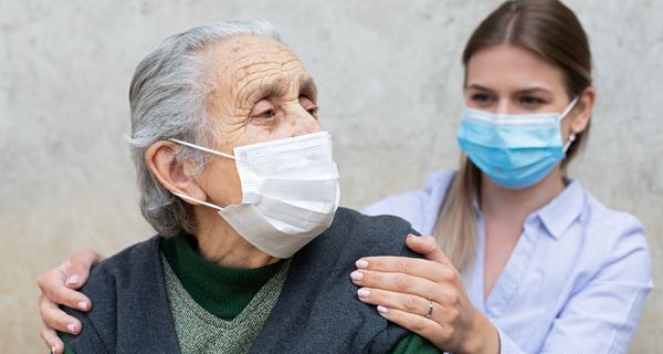 Seniorin und Pflegerin, beide tragen eine Maske.