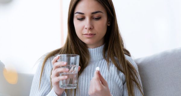 Junge Frau, hält ein Glas Wasser und eine Tablette in der Hand.