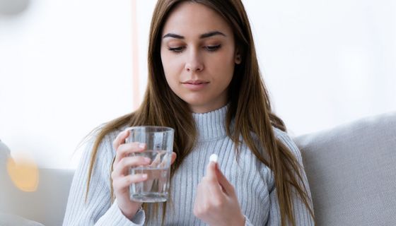 Junge Frau, hält ein Glas Wasser und eine Tablette in der Hand.