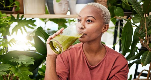 Junge Frau trinkt eiweißreichen Smoothie aus grünem Gemüse.