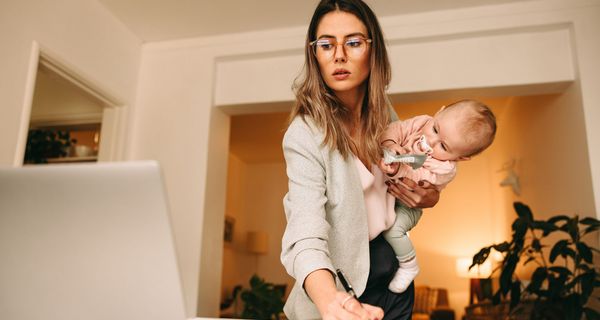 Frau, arbeitet und hält ein Baby auf dem Arm.