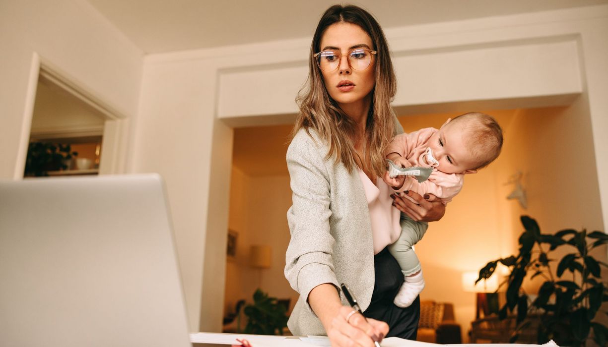 Frau, arbeitet und hält ein Baby auf dem Arm.