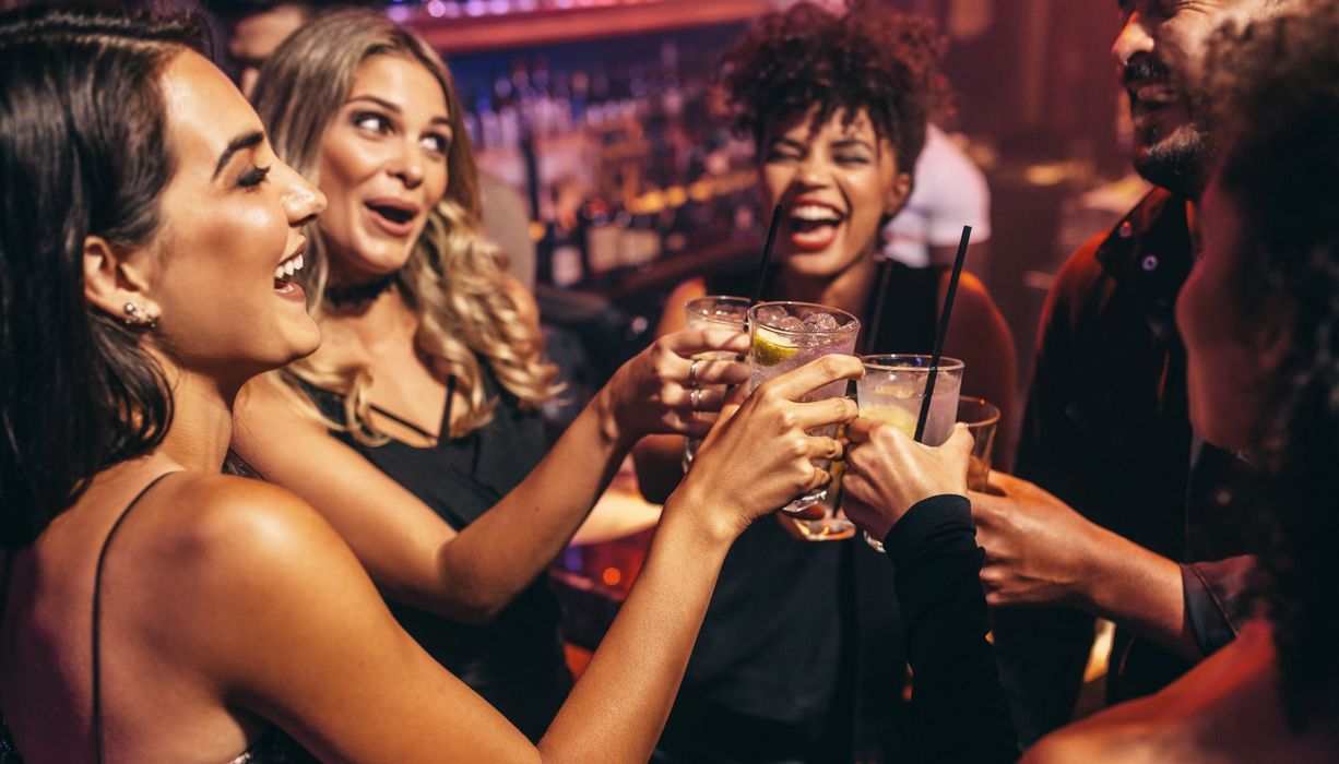 Vier junge Frauen und ein Mann stoßen mit Cocktails an. 