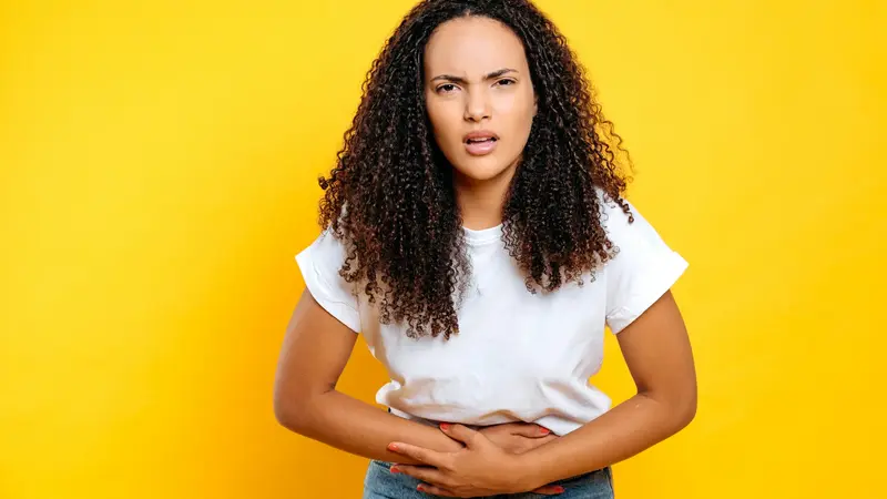 Junge Frau hält sich den Bauch und schaut genervt.