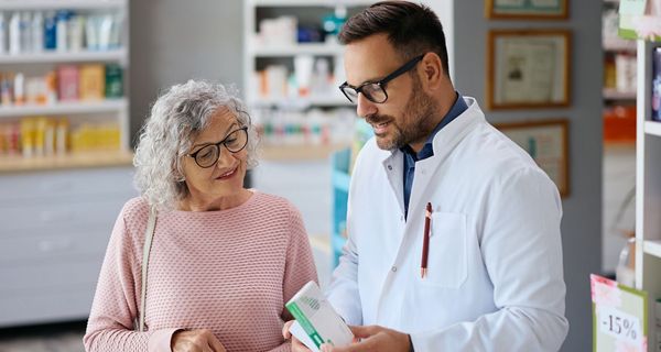 Ein Apotheker berät eine ältere Kundin zu einem Medikament.