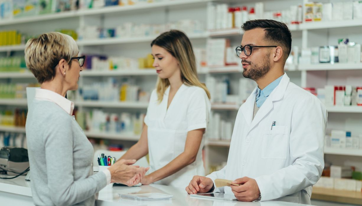 Ältere Frau in der Apotheke im Gespräch mit einem Apotheker.