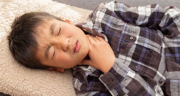 Junge, etwa acht Jahre alt, fasst sich an den Hals.