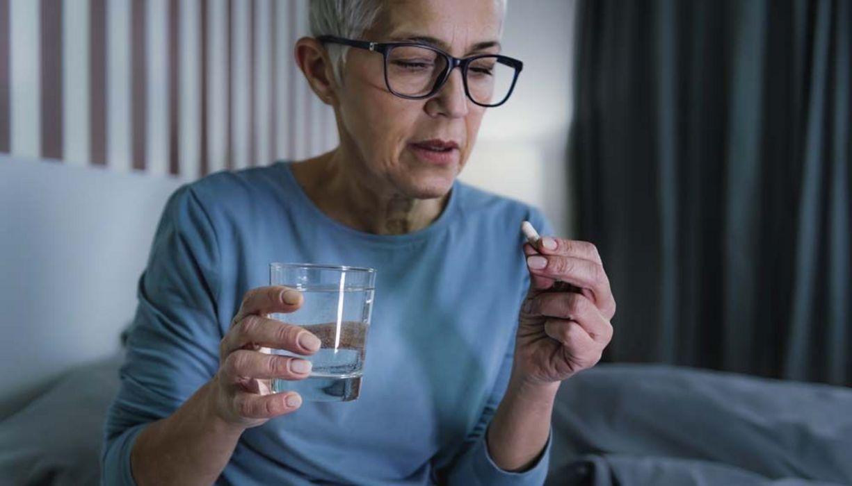 Ältere Frau, hält ein Glas Wasser und eine Tablette in der Hand. 