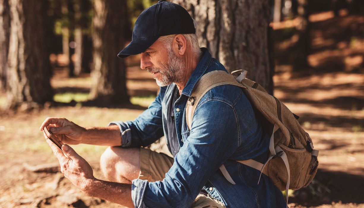 Älterer Mann mit Smartphone im Wald.