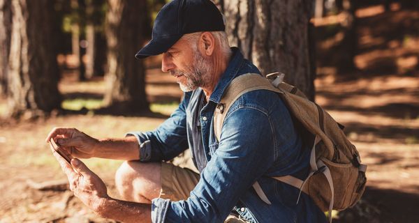 Älterer Mann mit Smartphone im Wald.