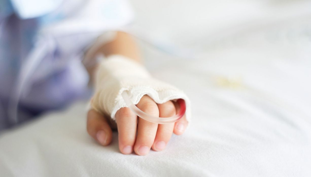 Hand von einem kleinen Kind, mit Zugang in einem Krankenhausbett.