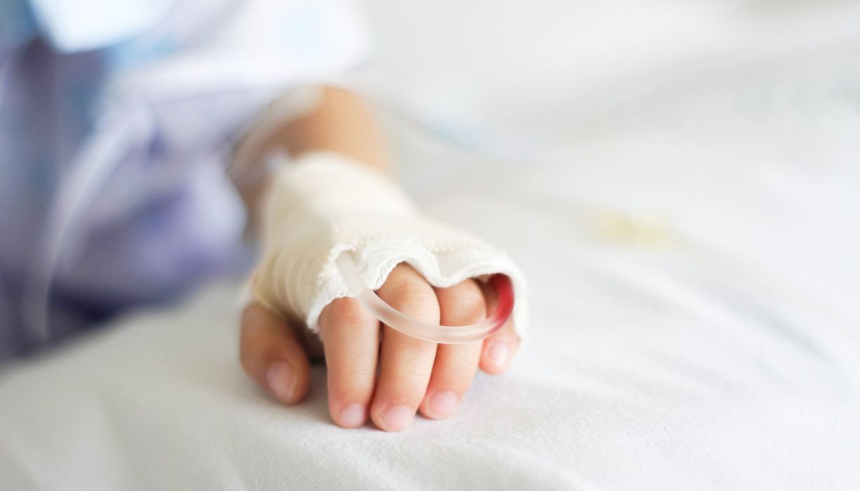 Hand von einem kleinen Kind, mit Zugang in einem Krankenhausbett.