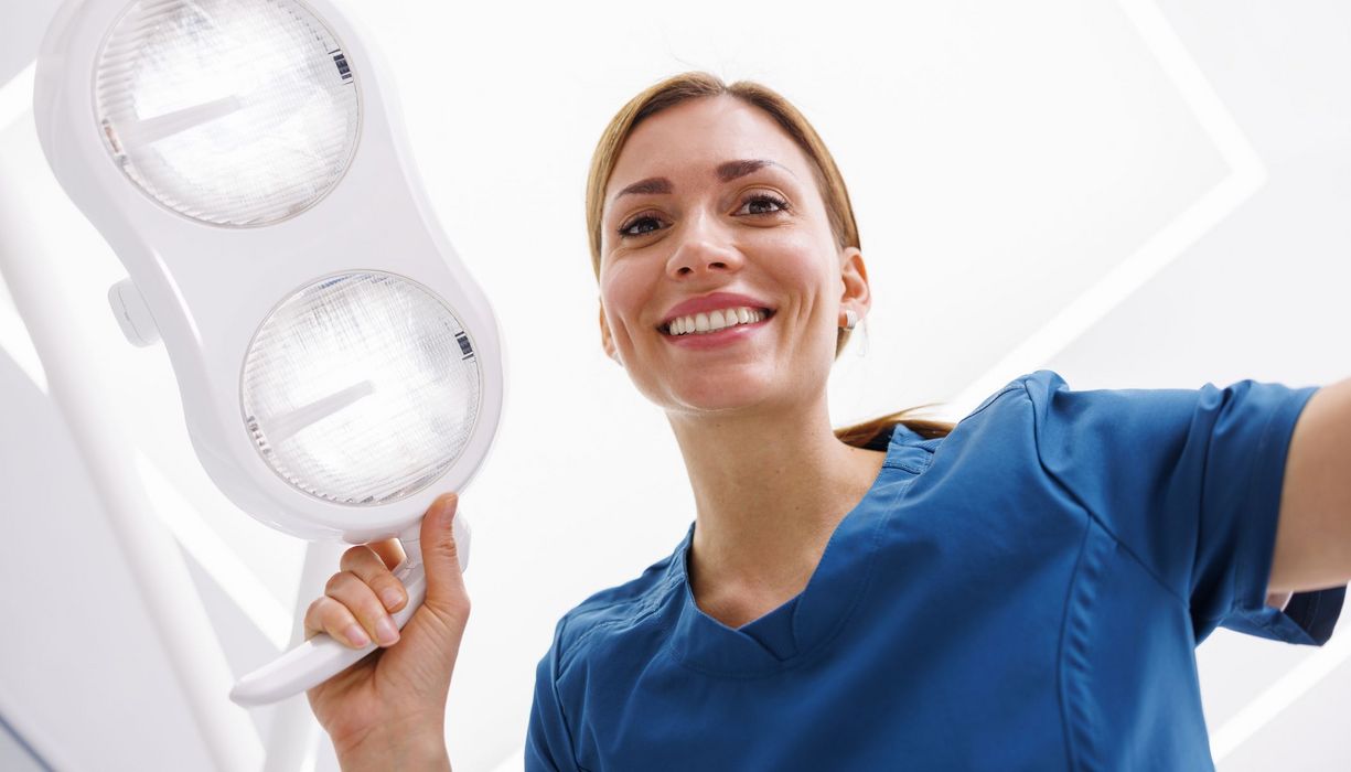 Junge Zahnarzthelferin, richtet die Lampe auf den zu behandelnden Patienten.