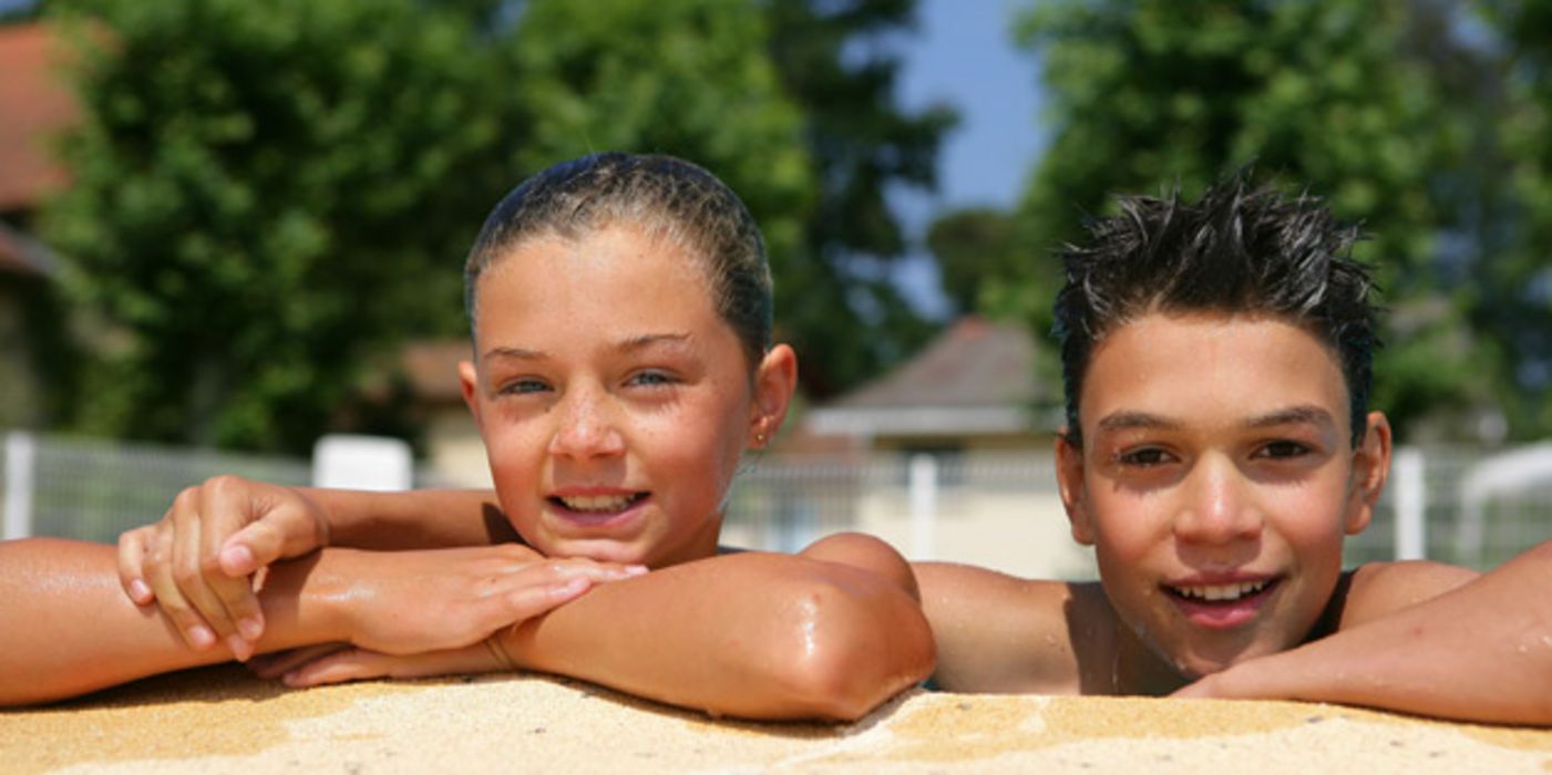 Zwei Kinder am Beckenrand eines Schwimmbads.